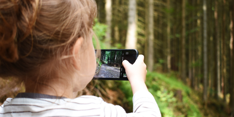 Photo of a young child in nature taking a picture on a smartphone